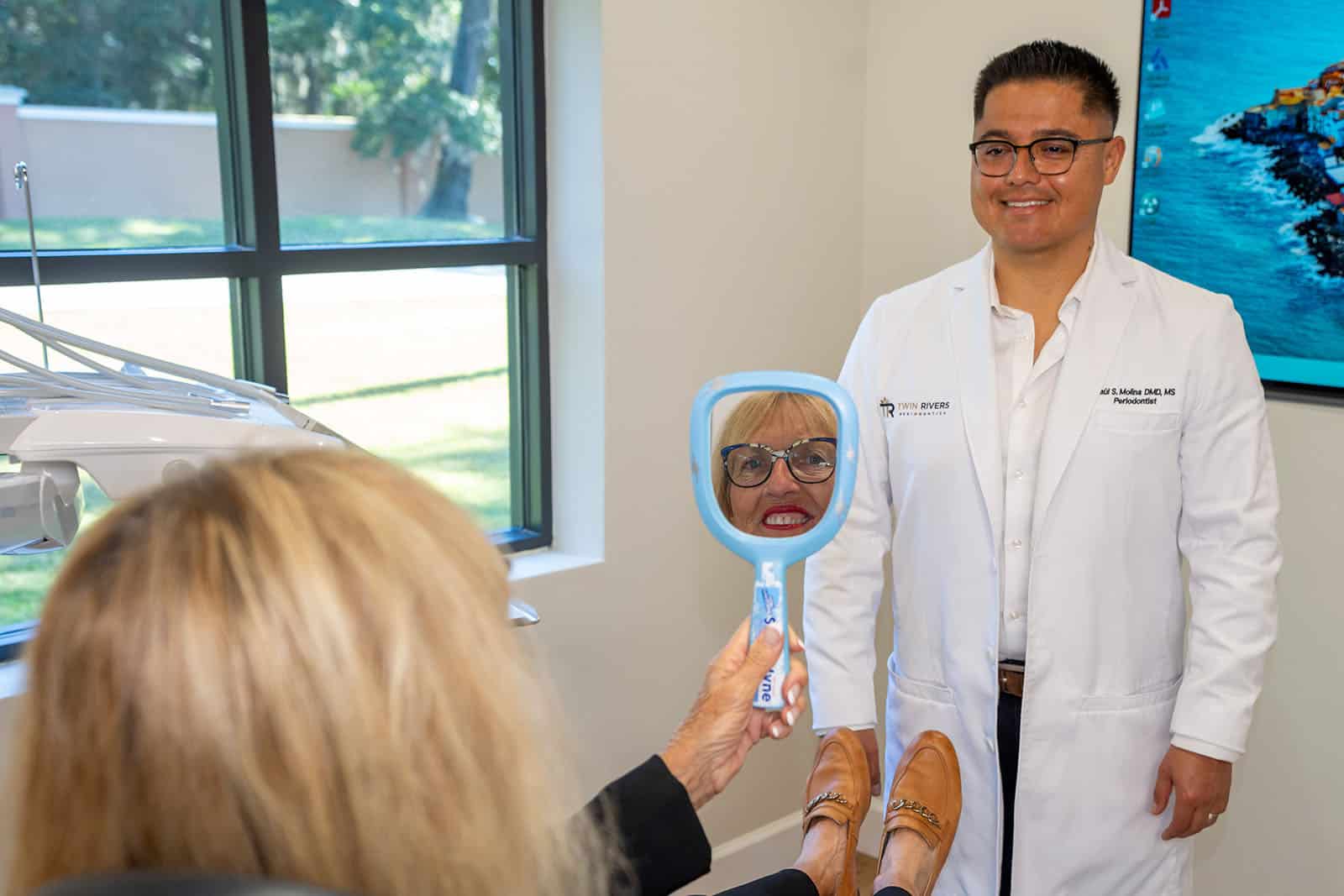 A patient checks her smile while Dr. Molina looks on