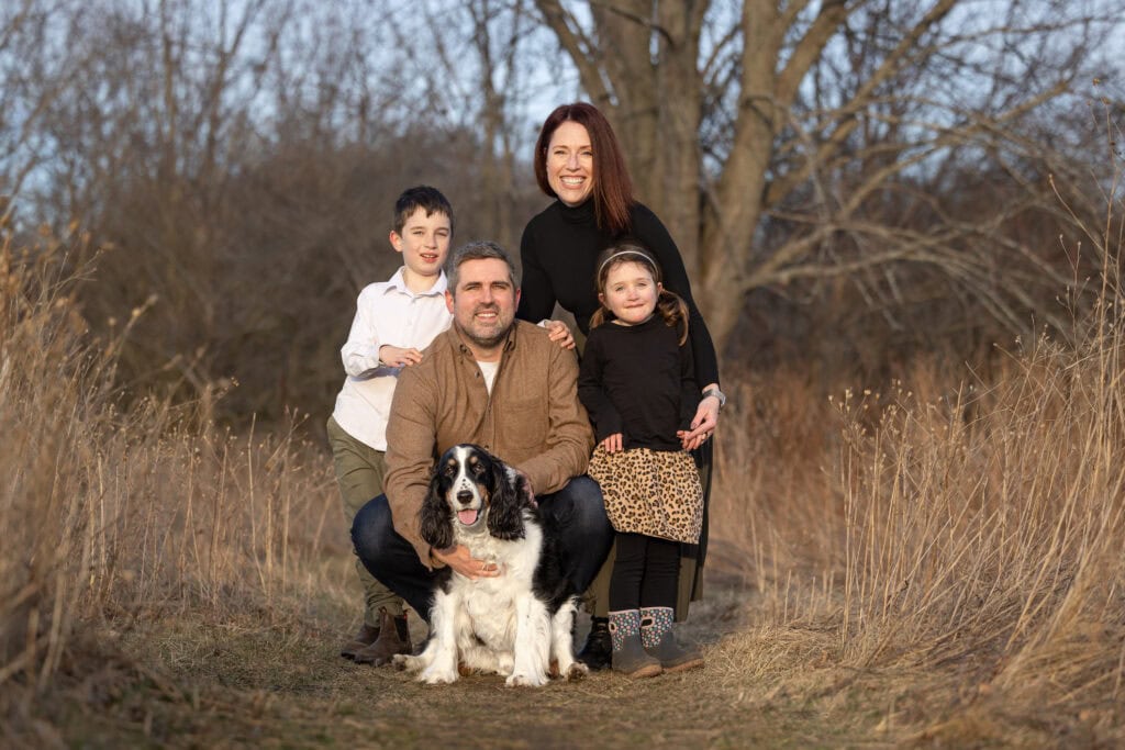 two children a mom and dad and their dog sitting in a field at Niagara Shores Park in Niagara on the Lake