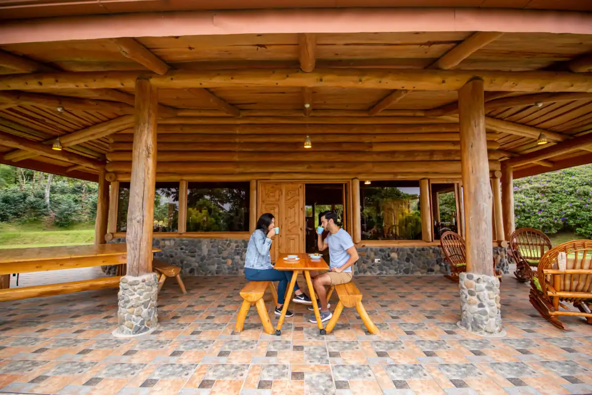 Dos personas conversan en una terraza de madera con vista a la naturaleza.