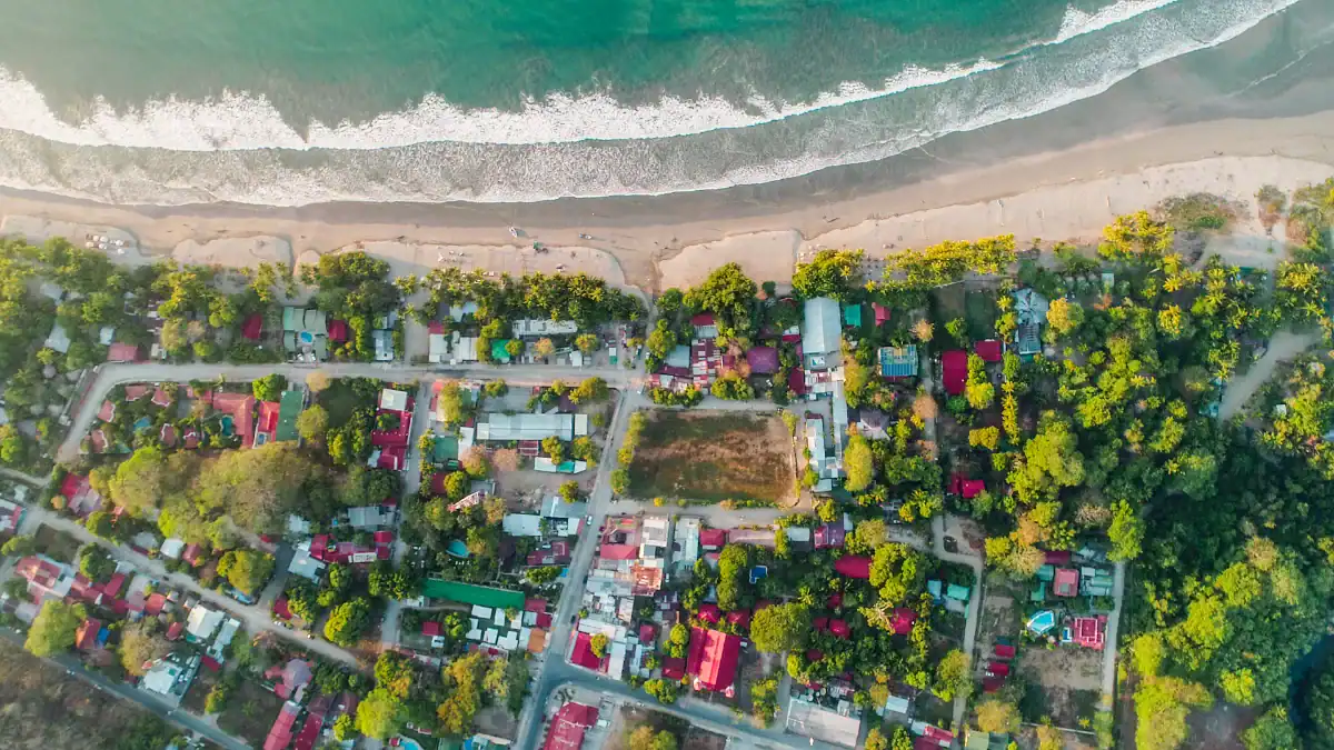 Vista aérea de un pueblo costero con casas coloridas y vegetación, junto a la playa y el mar.