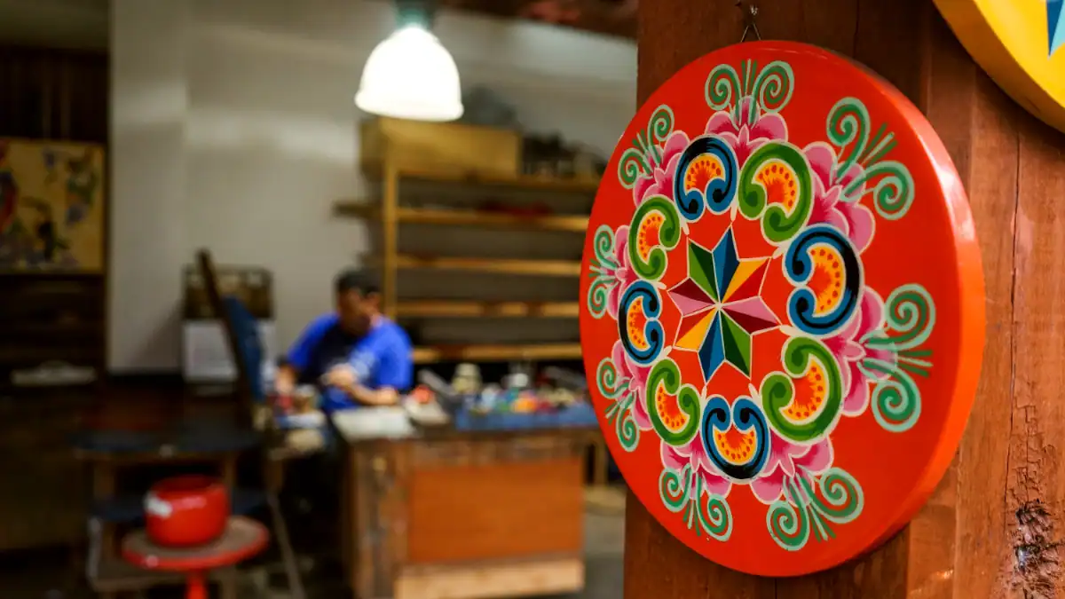 Decoración colorida de un plato de cerámica con patrones florales y geométricos en un ambiente de taller.