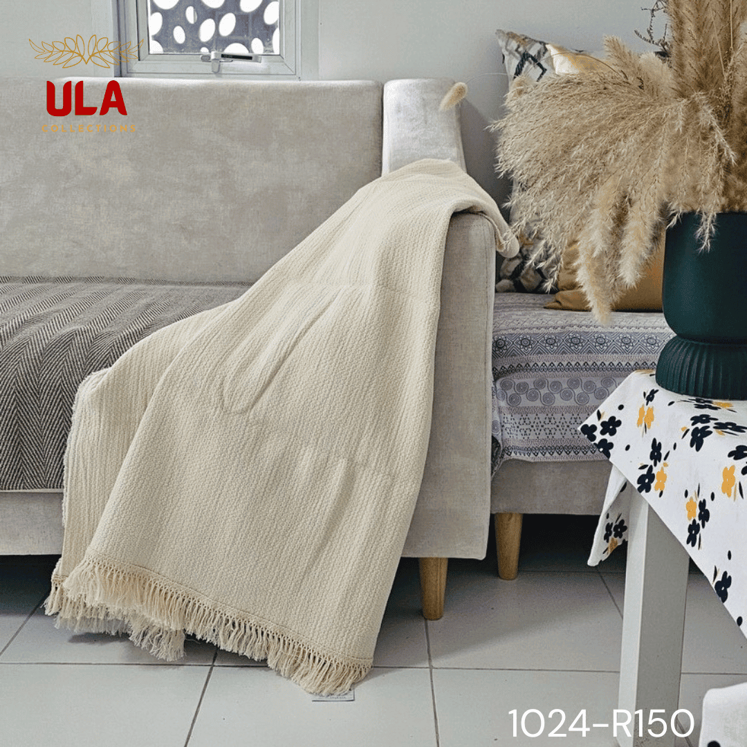 A view of a thick, chunky woven throw blanket in a natural cream or off-white color. The blanket features highly textured details, including vertical wavy ruched ruffles on the left and a wide natural-colored fringe along the bottom. The reverse side shows a simple, thick weave, highlighting its minimalist, bohemian, or modern farmhouse texture for home decor.