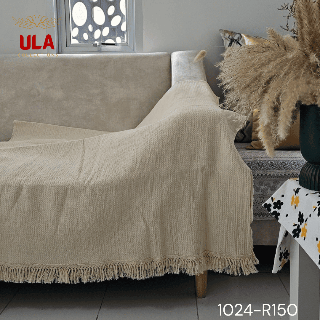 A view of a thick, chunky woven throw blanket in a natural cream or off-white color. The blanket features highly textured details, including vertical wavy ruched ruffles on the left and a wide natural-colored fringe along the bottom. The reverse side shows a simple, thick weave, highlighting its minimalist, bohemian, or modern farmhouse texture for home decor.