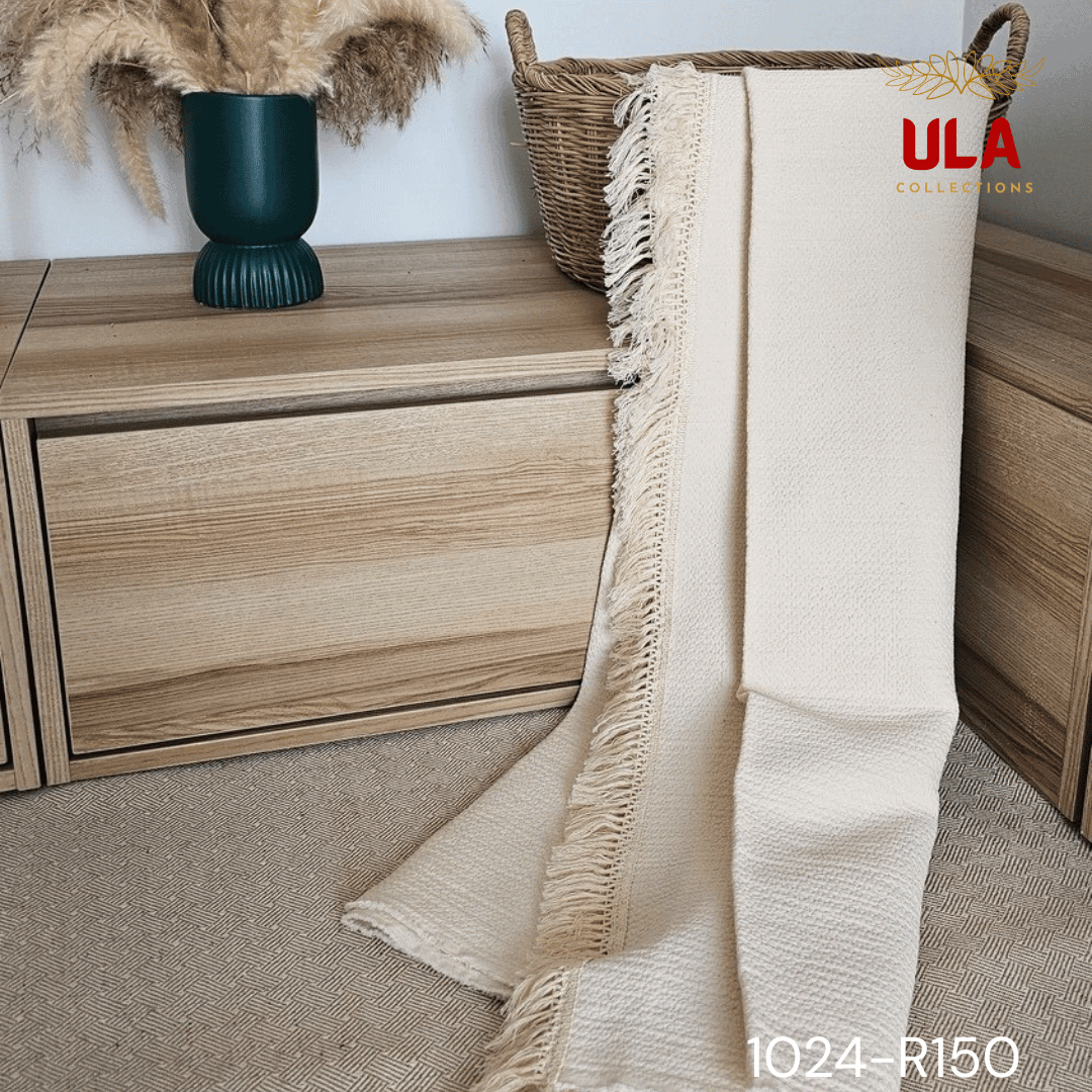 A view of a thick, chunky woven throw blanket in a natural cream or off-white color. The blanket features highly textured details, including vertical wavy ruched ruffles on the left and a wide natural-colored fringe along the bottom. The reverse side shows a simple, thick weave, highlighting its minimalist, bohemian, or modern farmhouse texture for home decor.