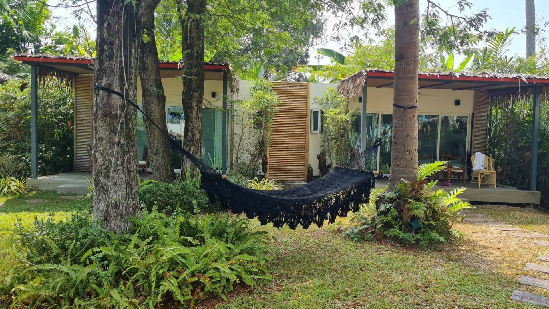 Black woven hammock with fringe hanging between trees outside rustic bungalow resort