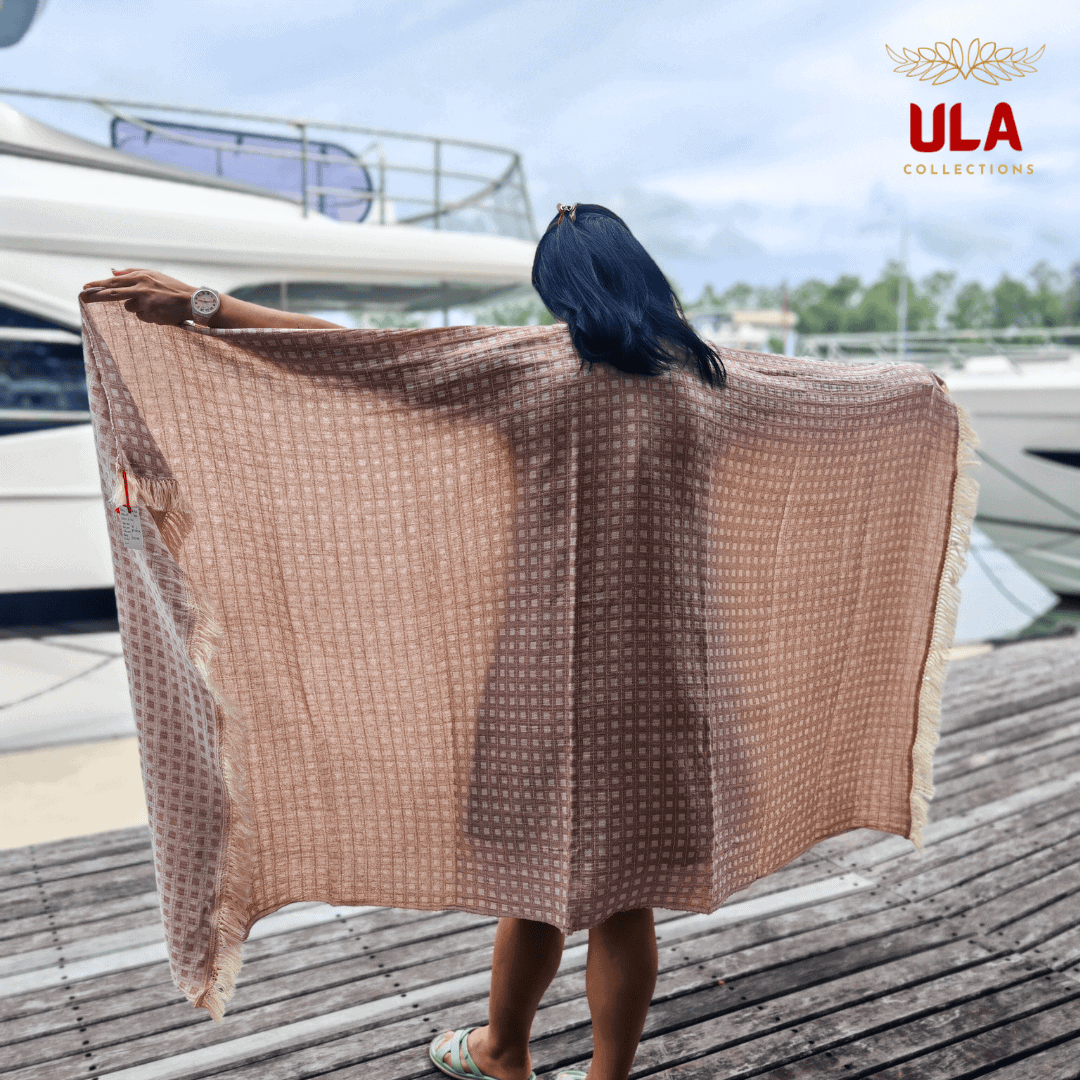 plum taupe throw blanket with white square check pattern, worn as a shawl by a woman on a marina pier with white yachts in the background.