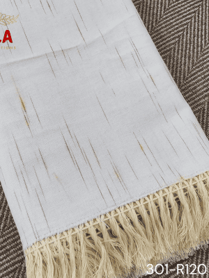 A close-up view of a white woven throw blanket or textile featuring a subtle, vertically dashed Ikat pattern in a thin gold or light brown thread. The blanket is finished with a wide natural beige tassel fringe and is accented with a delicate woven trim.