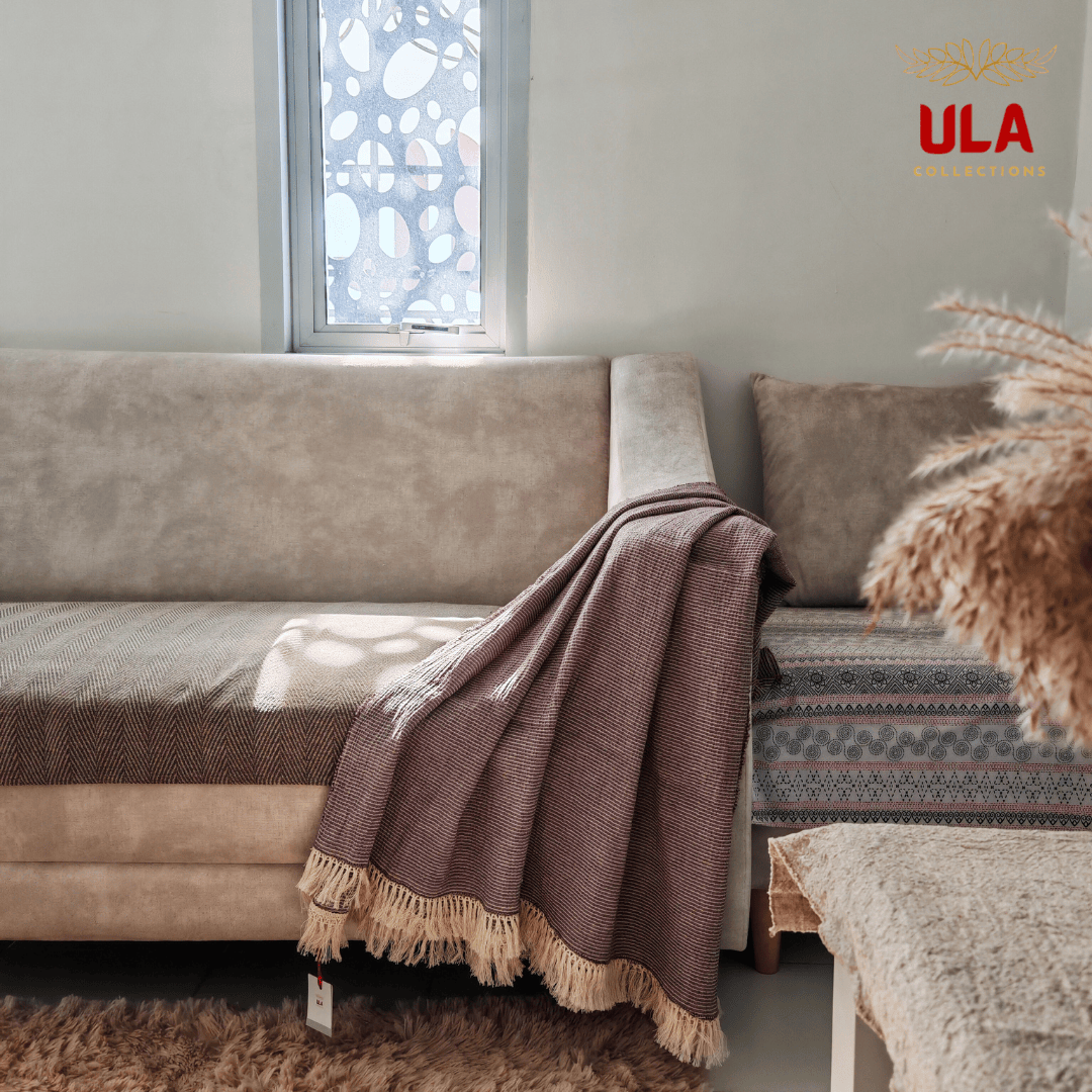 Muted purple textured cotton throw blanket with fringe edges draped over a beige couch, cozy living room accent and soft textile by ULA Collections.