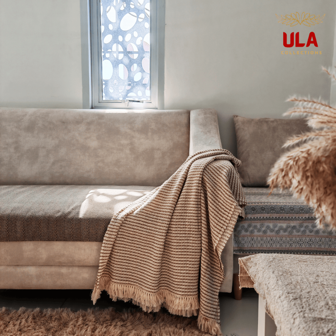 Warm red brown striped textured throw blanket with tassel edges draped on a beige couch, earthy interior decor by ULA Collections.