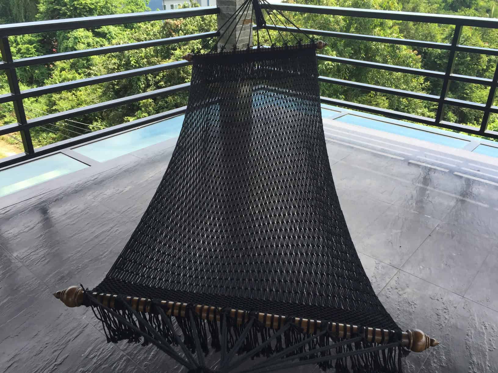 Luxury black rope hammock on a resort balcony with a tropical jungle and mountain view.