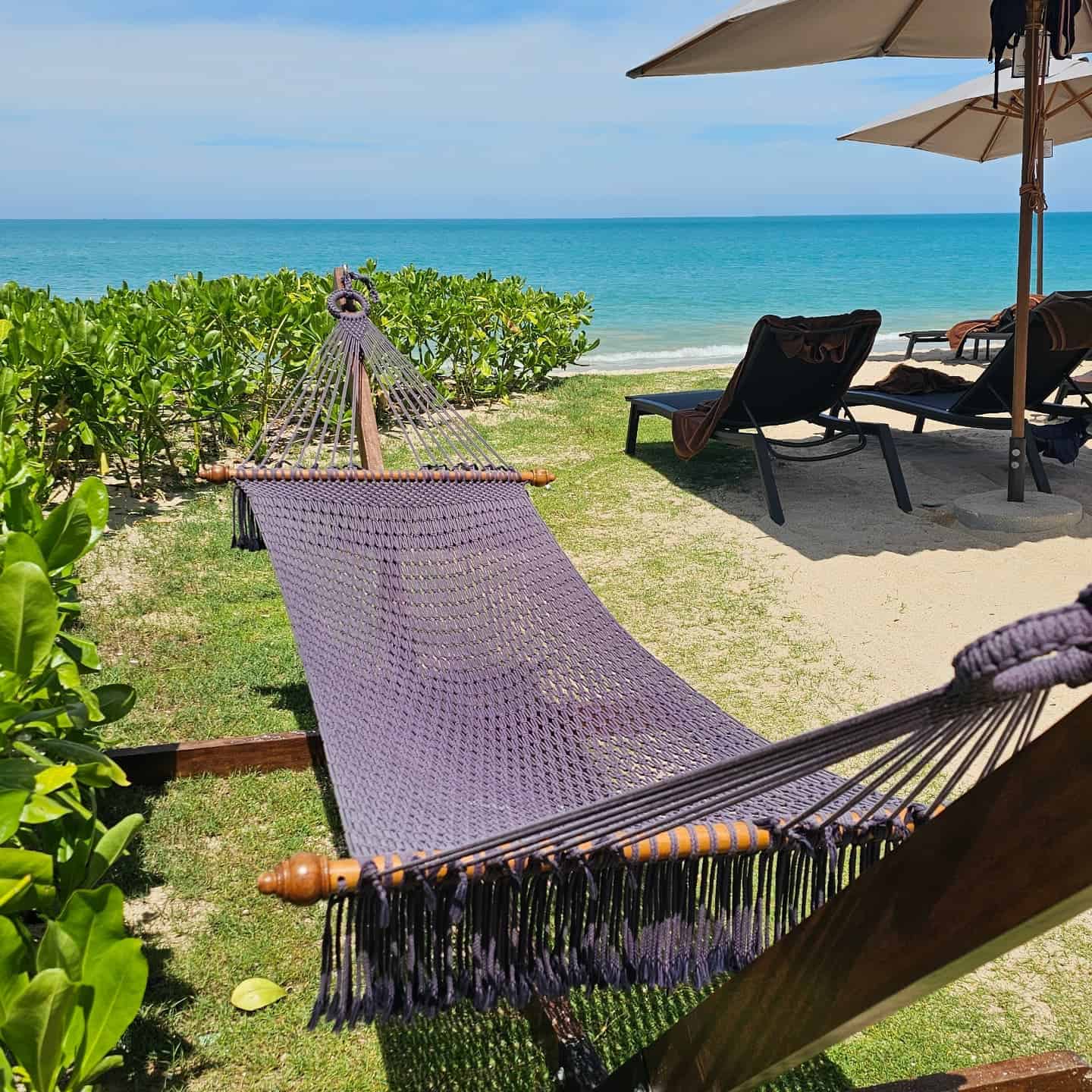 Outdoor purple/midnight blue rope hammock and stand on a tropical beachfront lawn.