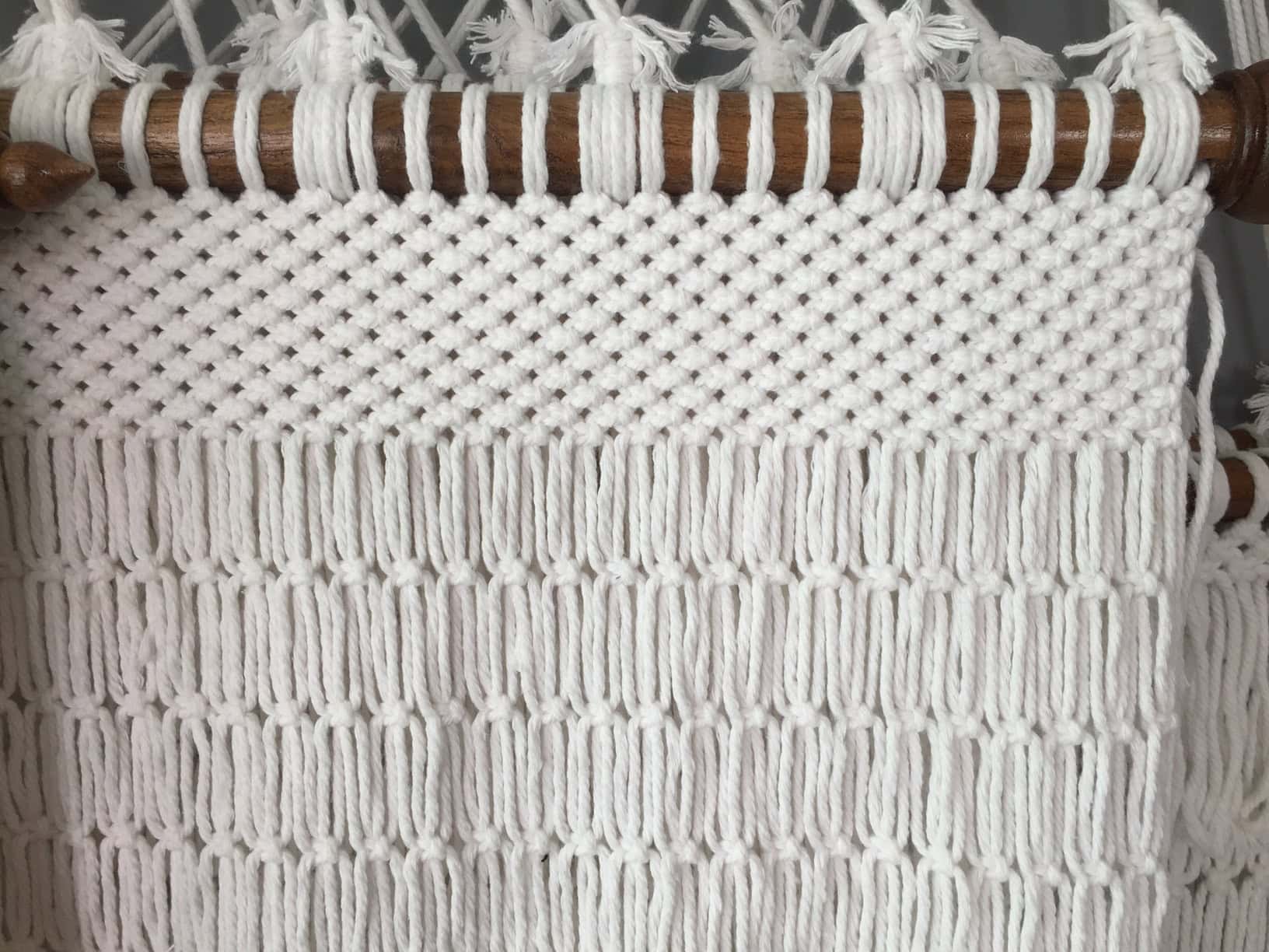 Close-up of a Bliss White macrame hammock showing the detailed white rope knot pattern and brown wood spreader bar.