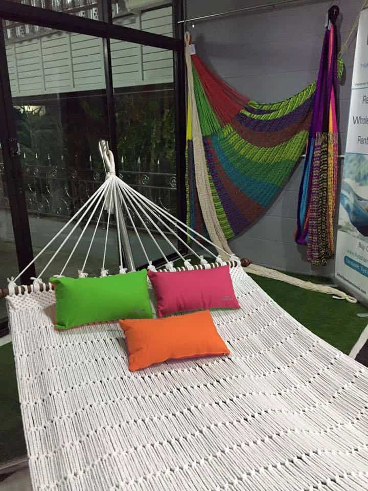 Indoor white rope hammock with wooden spreader bars and colorful cushions for home decor.