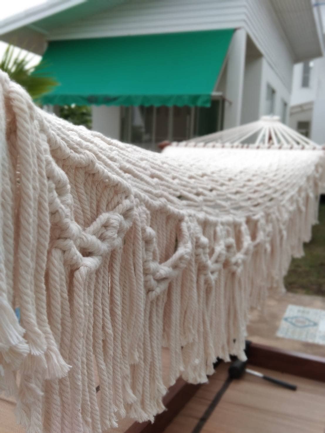 close-up beige cotton rope hammock with thick fringe and wooden ends.