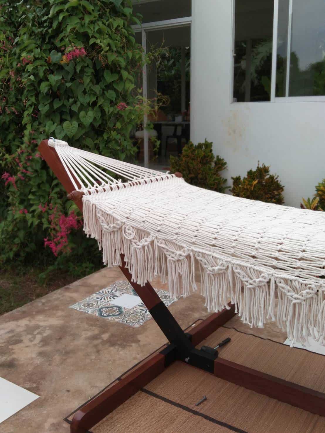 Outdoor beige fringe rope hammock and wooden stand for patio relaxation.