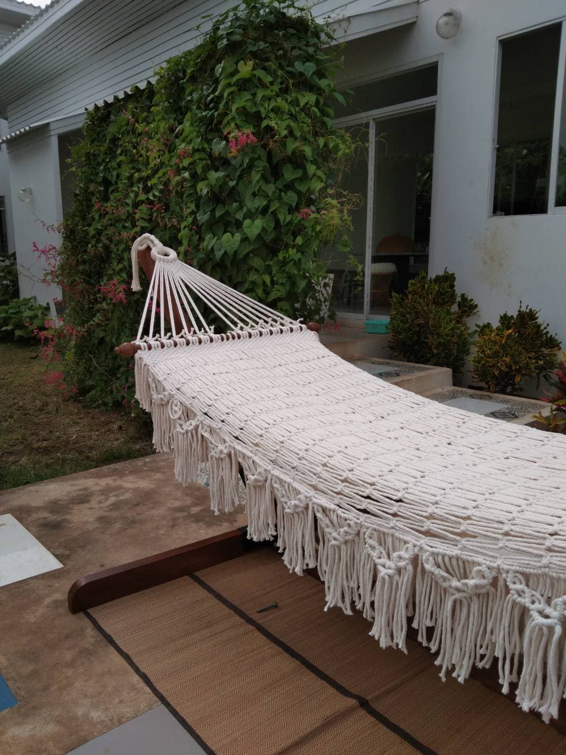 Outdoor beige fringe rope hammock and wooden stand for patio relaxation.