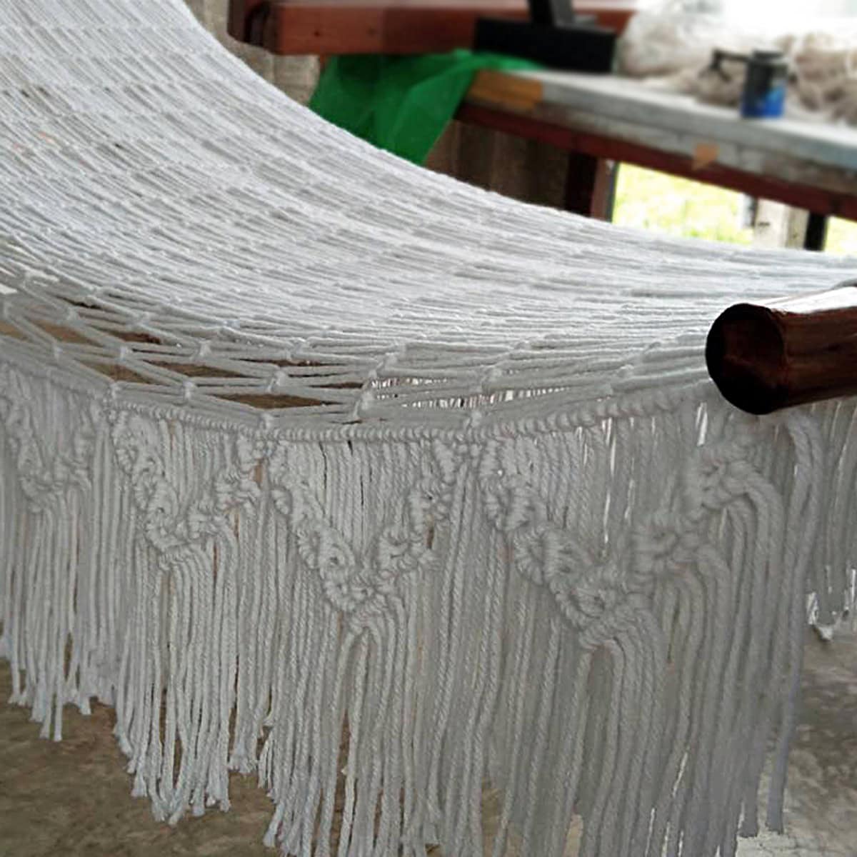 Close-up outdoor beige cotton rope hammock with thick fringe and wooden ends.