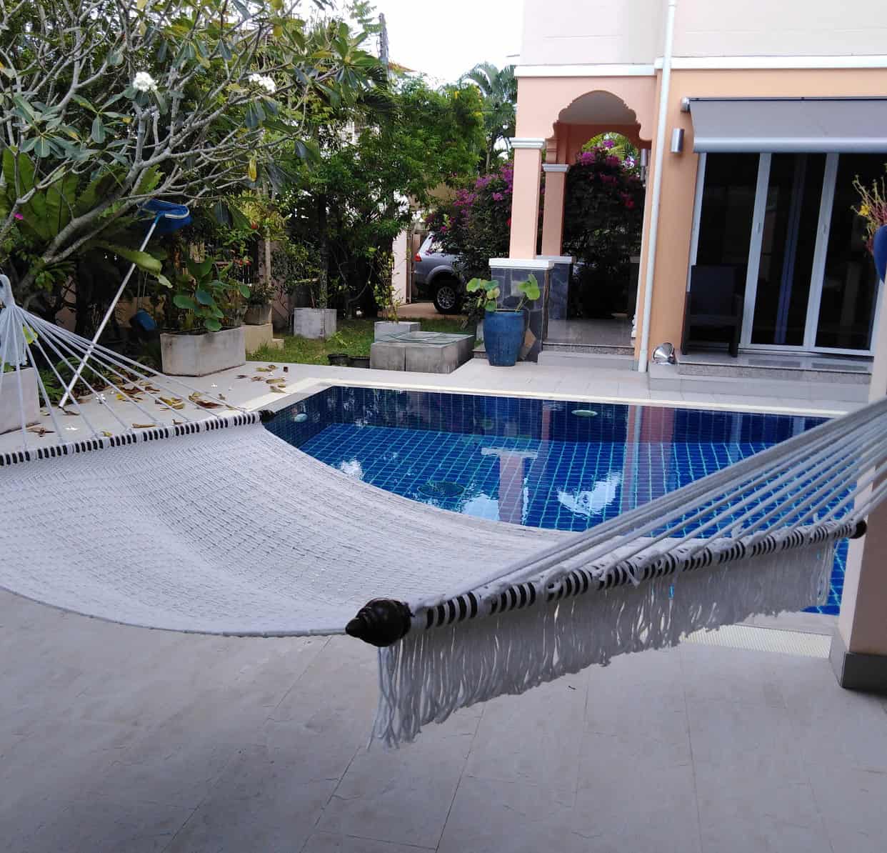 Outdoor beige rope hammock hanging over a patio by a swimming pool.
