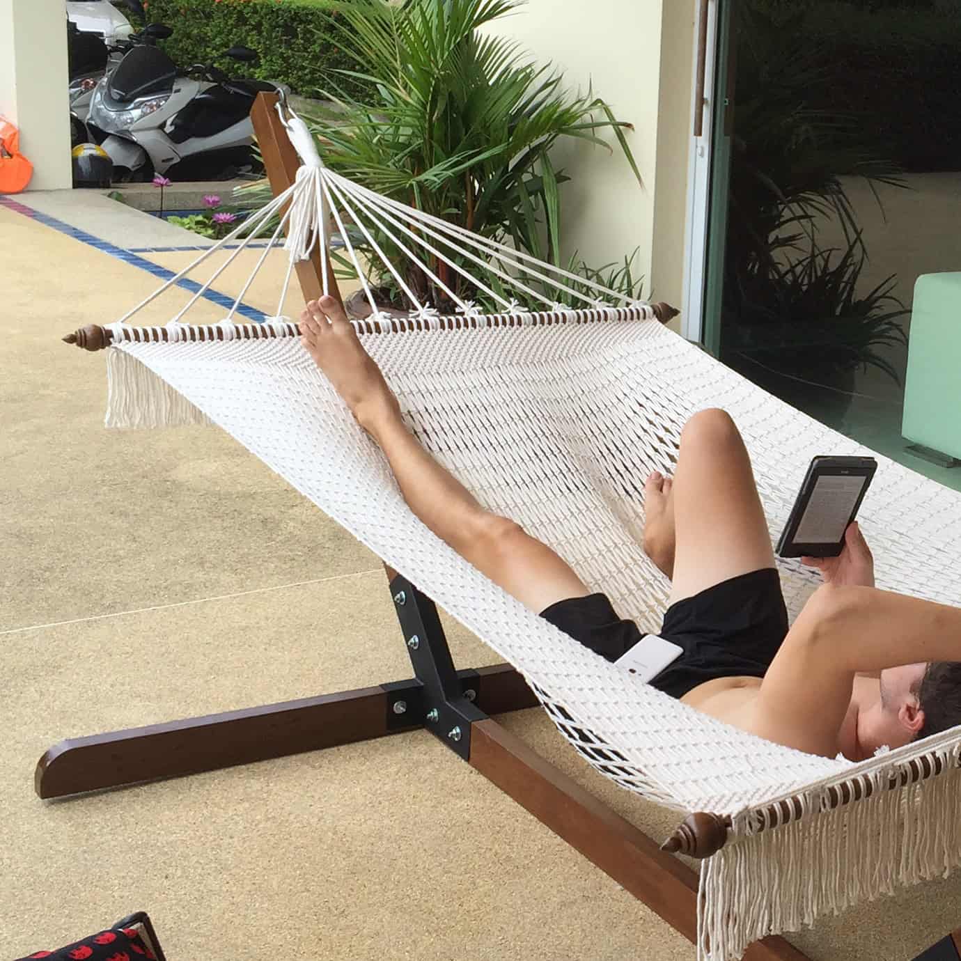 Outdoor white rope hammock on a wooden stand for reading and patio relaxation.