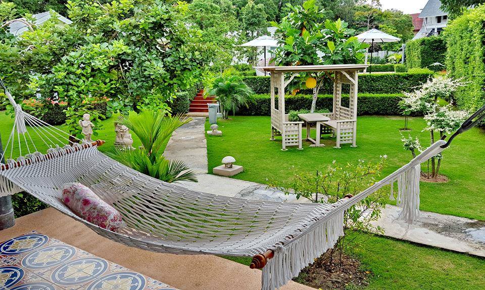 Outdoor lifestyle image showing a fringed white rope hammock on a patio with a tropical garden, perfect for backyard relaxation.