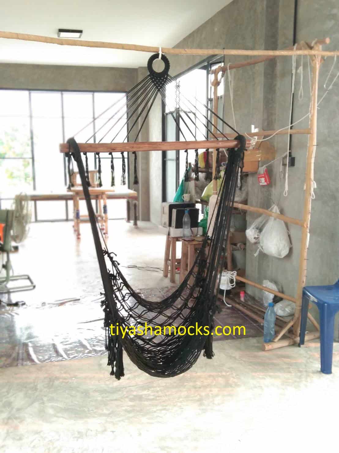 Black macrame "Pausa" hanging chair with wooden bar, relaxing in a minimalist, industrial-style interior or workshop setting.