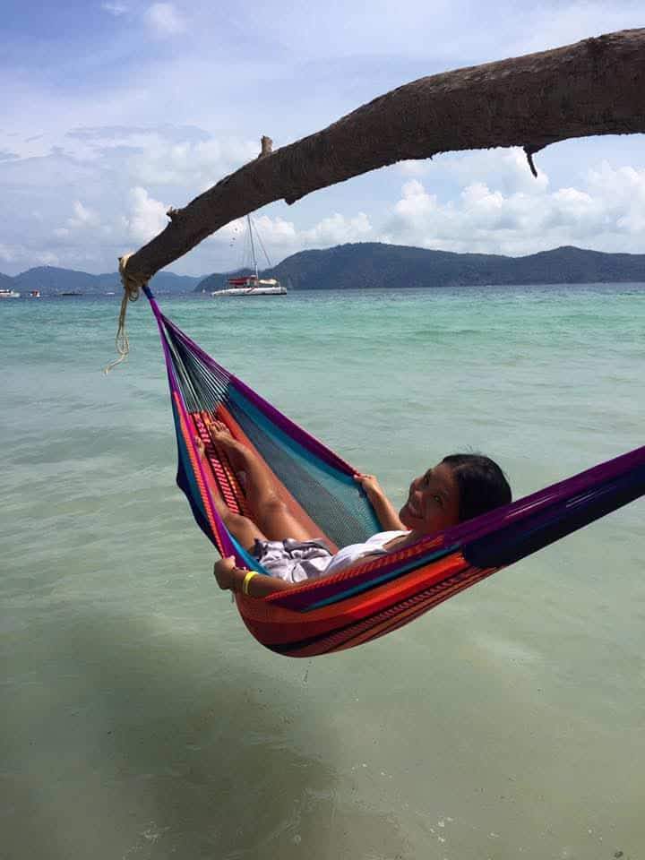 Close-up of a person relaxing in a colorful striped hammock hanging over the sea at a tropical island.