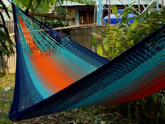 Woven net hammock chair, "Ranong" pattern, featuring alternating bold stripes of deep blue, bright teal, and vivid orange, suggesting a tropical sunset over the ocean.