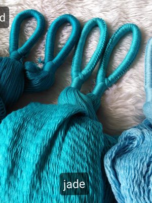 Travel_blue_mallard_jade_tropical_low A close-up of different colored woven fabric swatches and hanging loops, likely from hammocks, against a white furry background. The colors are labeled: mallard (dark teal), jade (bright turquoise), and tropical (light blue), highlighting the variety of vibrant colors available for outdoor leisure products.