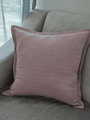 Square throw pillow in solid blush pink cotton with subtle stitched horizontal stripes on a gray sofa
