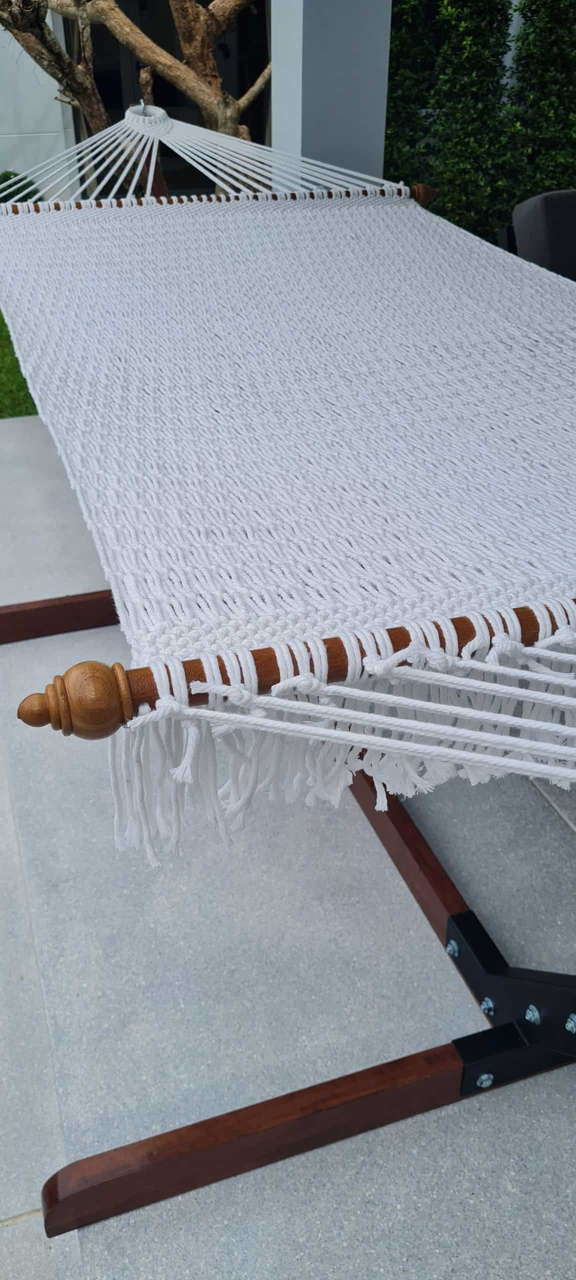 close-up white rope hammock with a wood stand beside a swimming pool and luxury villa patio