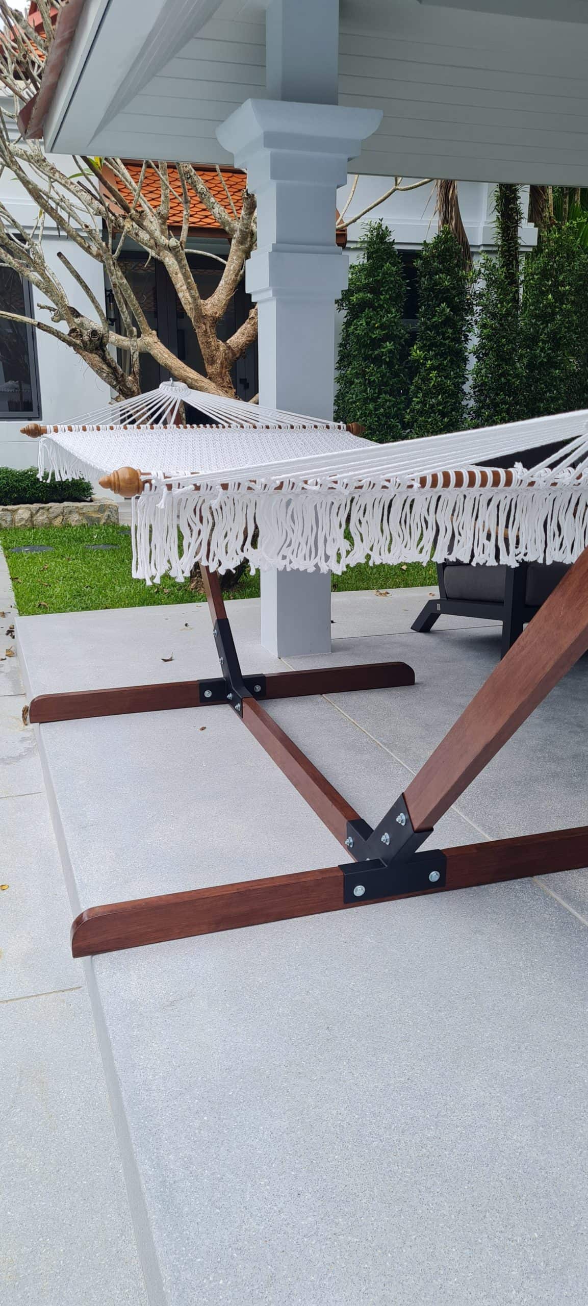 White rope hammock with a wood stand beside a swimming pool and luxury villa patio
