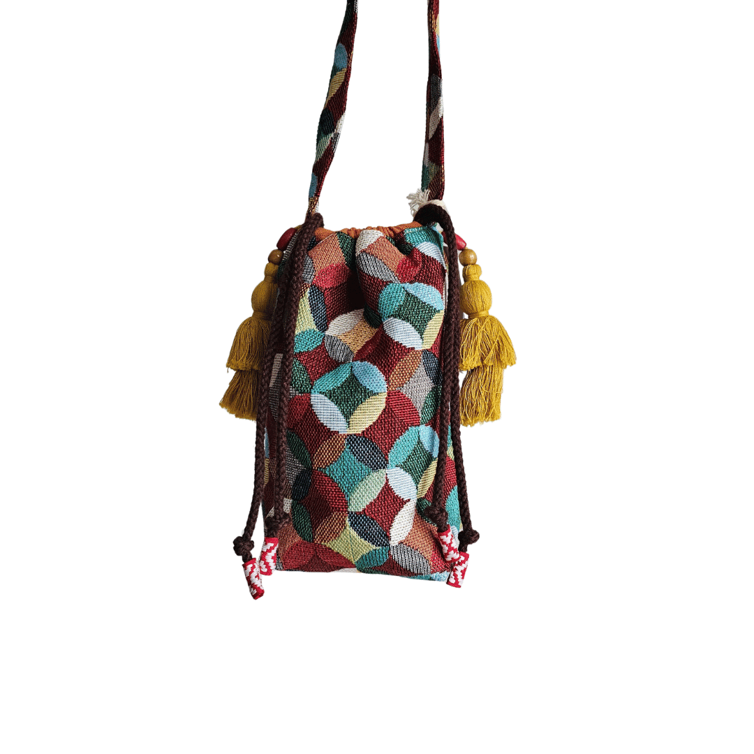 A stylish drawstring bucket bag or pouch bag featuring a vibrant, multi-color geometric fabric pattern with interlocking circle or Seigaiha wave motifs with bohemian style. The textile includes shades of teal, burgundy, olive green, cream, and brown. Decorated with tassels and wood beats