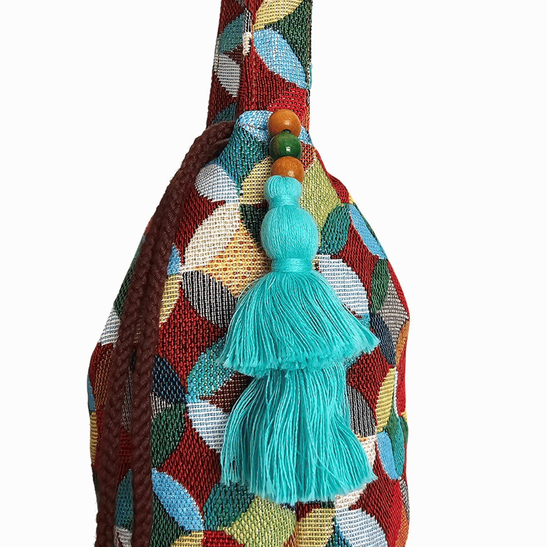 A stylish drawstring bucket bag or pouch bag featuring a vibrant, multi-color geometric fabric pattern with interlocking circle or Seigaiha wave motifs with bohemian style. The textile includes shades of teal, burgundy, olive green, cream, and brown. Decorated with tassels and wood beats