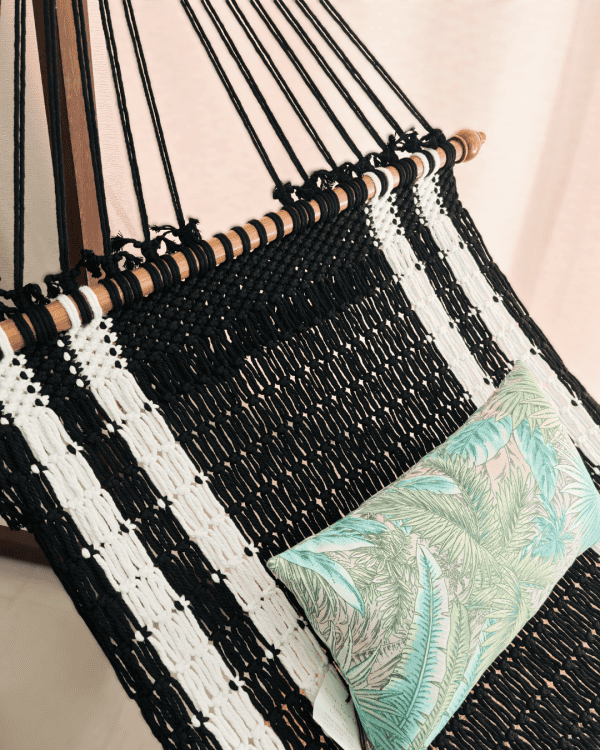 Close-up of the woven black and white rope hammock, wooden spreader bar, and the tropical leaf lumbar pillow