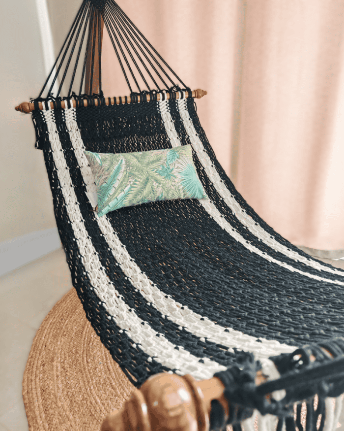 Handmade black and white striped cotton rope hammock with wooden spreader bars and a tropical print pillow