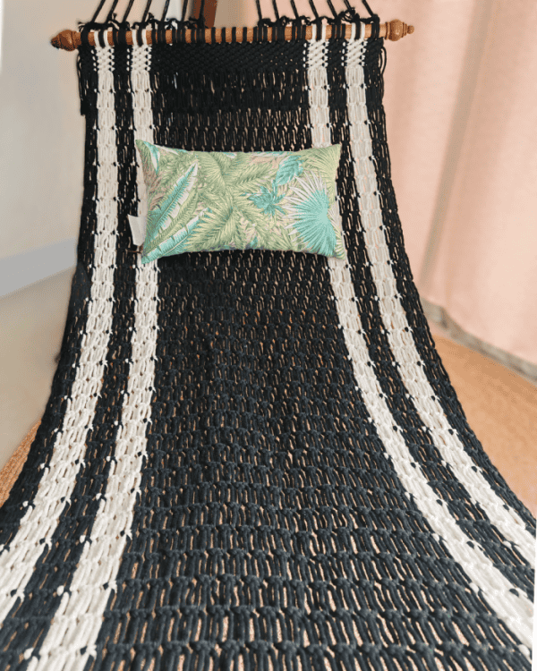 Full view of the black and white stripe woven rope hammock with a green tropical leaf pattern pillow