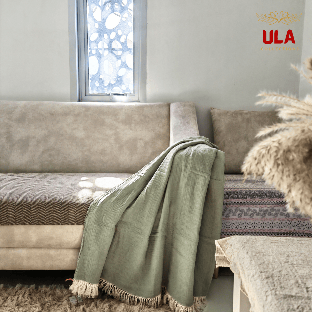 Green-colored Sage double layer salu throw blanket with tassel trim on a neutral couch, minimalist living room aesthetic by ULA Collections.