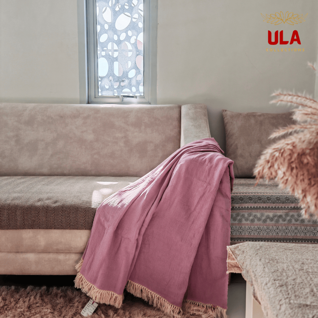 Purple-colored First Blush double layer salu throw blanket with tassel trim on a neutral couch, minimalist living room aesthetic by ULA Collections.