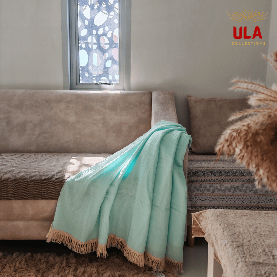 Blue-colored Light Blue double layer salu throw blanket with tassel trim on a neutral couch, minimalist living room aesthetic by ULA Collections.