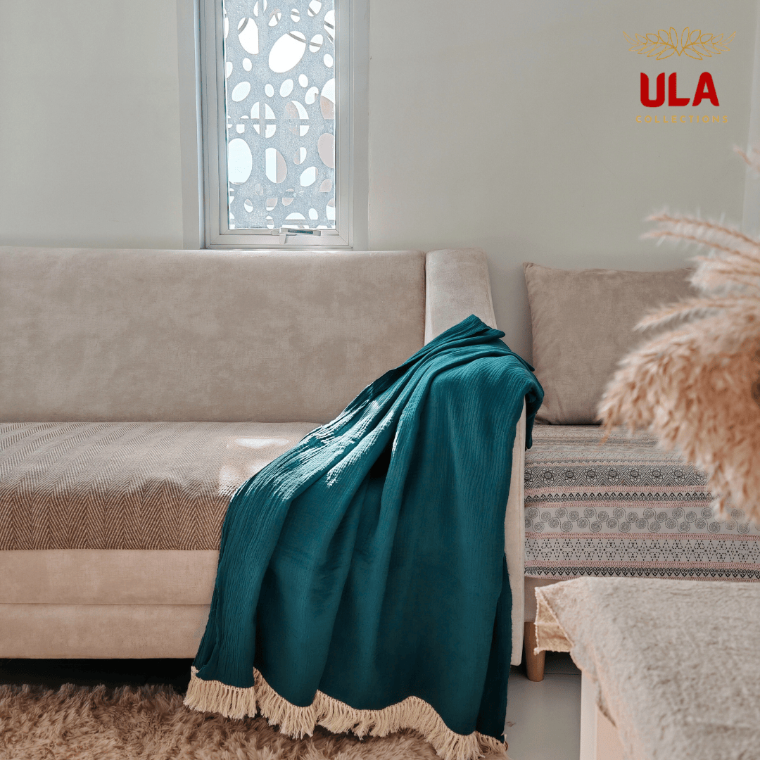 Green-colored Marine double layer salu throw blanket with tassel trim on a neutral couch, minimalist living room aesthetic by ULA Collections.