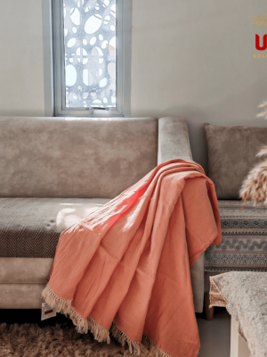 Peach double layer sulu textured cotton throw blanket with fringe edges draped over a beige modern sofa, home decor styling by ULA Collections.