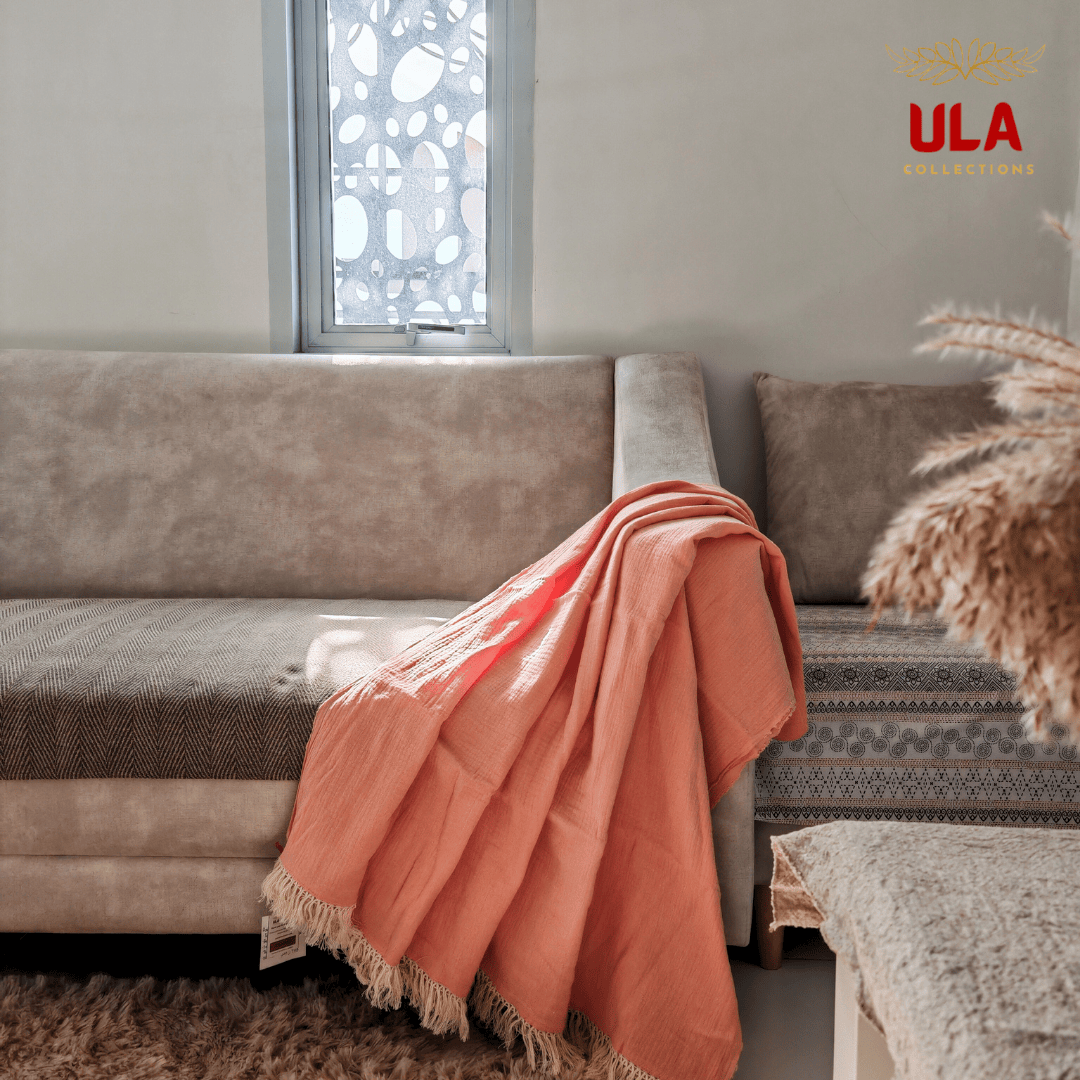 Peach double layer sulu textured cotton throw blanket with fringe edges draped over a beige modern sofa, home decor styling by ULA Collections.