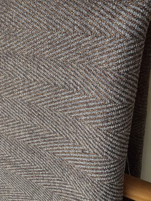High-texture, dual-color woven fabric featuring a classic herringbone or chevron pattern, draped over a wooden rail, ideal for durable sofa or chair upholstery.