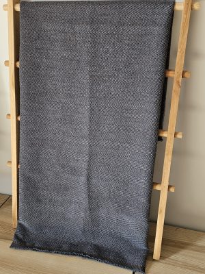 Full view of thick, dark grey and brown herringbone throw blanket or fabric piece hanging on a light wooden display ladder in a modern home setting.
