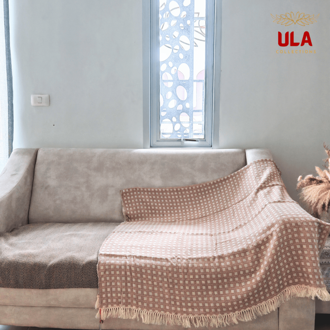 plum taupe woven throw blanket with white square check pattern and fringe, draped over a neutral beige sofa.