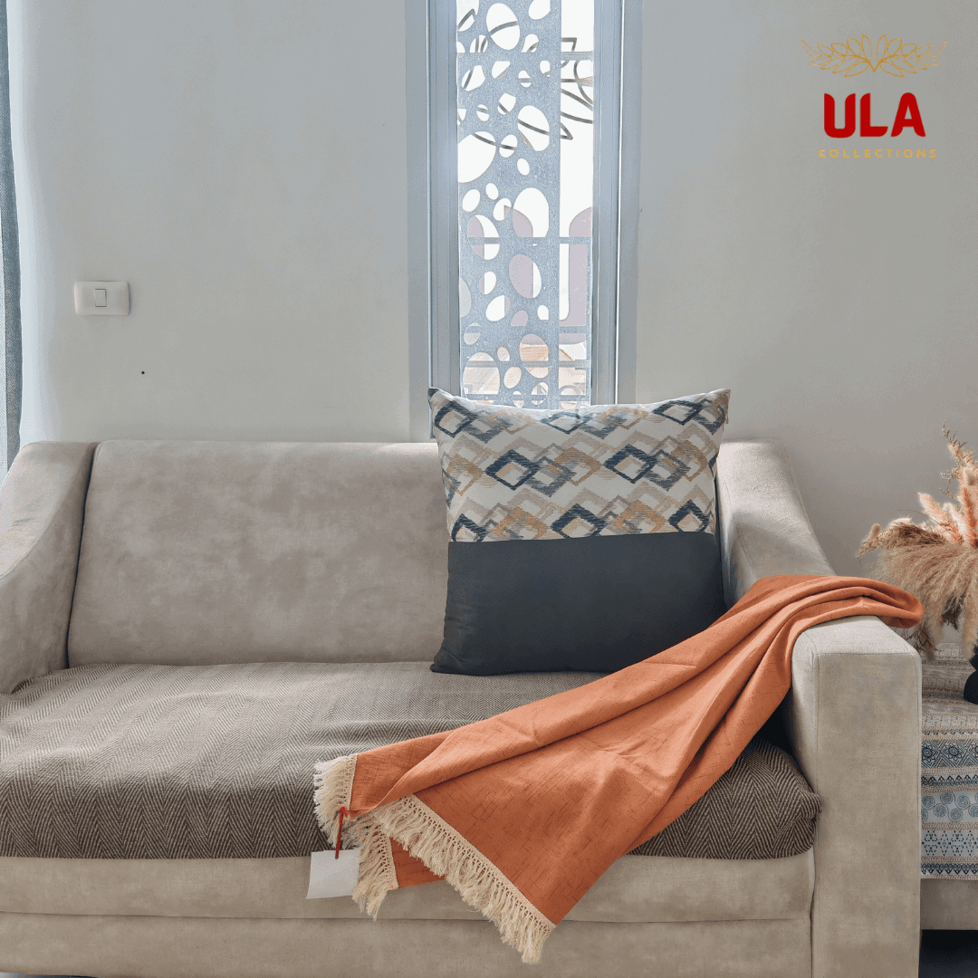 orange throw blanket draped over a beige sofa with a geometric accent pillow and brown herringbone blanket.