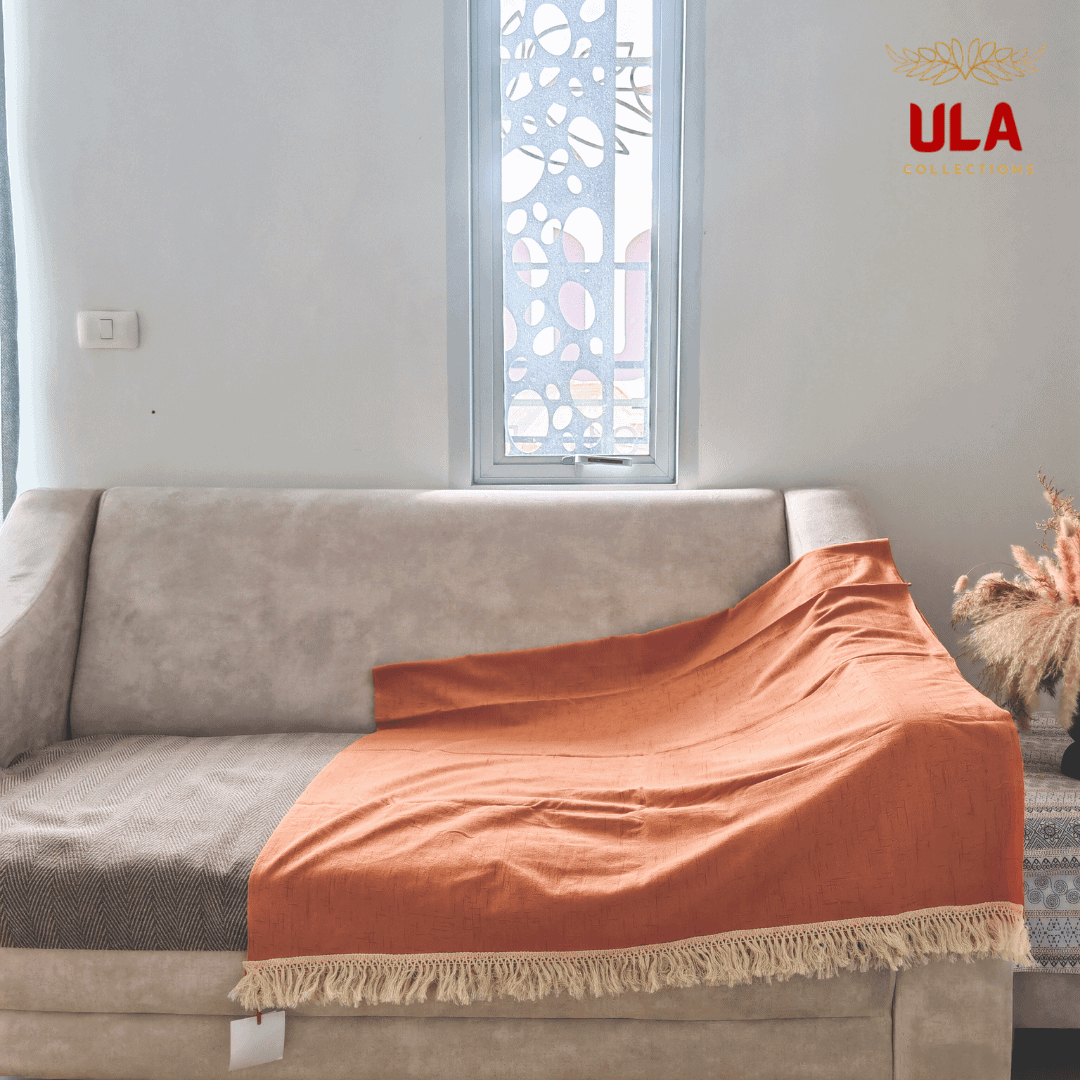 rustic burnt orange throw blanket with white fringe, draped across a light beige sofa with a brown herringbone throw underneath.
