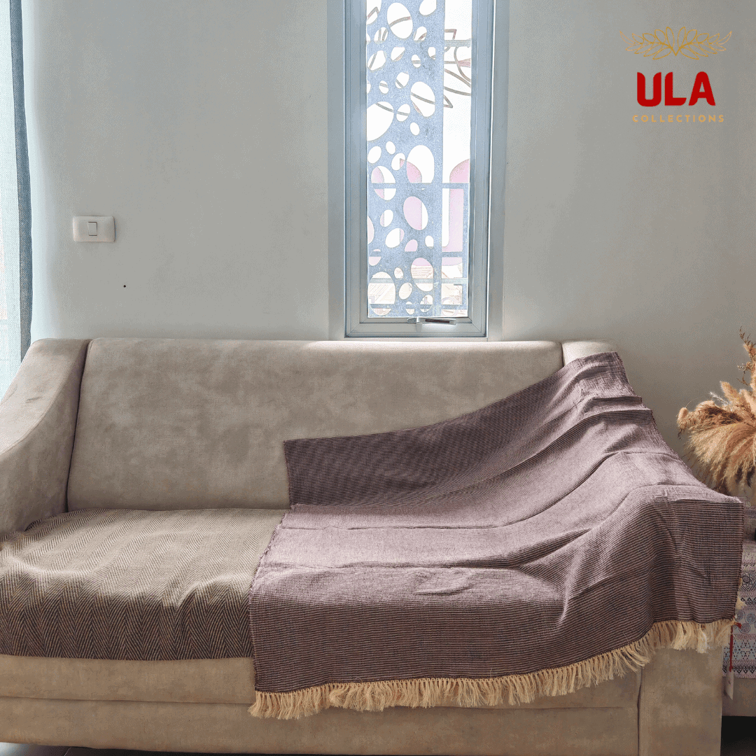 solid plum/mauve textured throw blanket with light fringe, draped over a neutral beige sofa with a brown herringbone cushion cover.