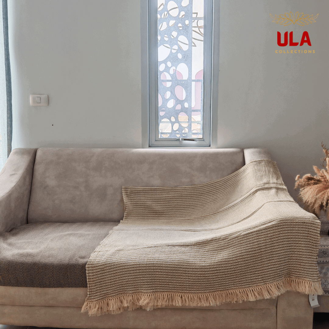 striped woven throw blanket in cream with thin olive green horizontal stripes and fringe, draped over a neutral beige sofa.