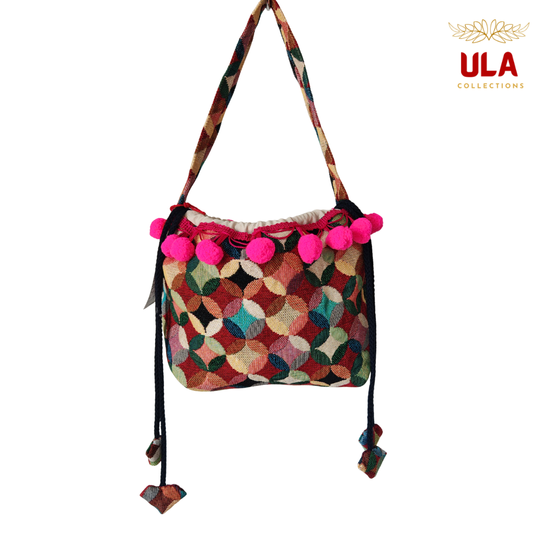 woven colorful patchwork drawstring bag, viewed straight on, featuring hot pink pom-poms and thick braided drawstrings.